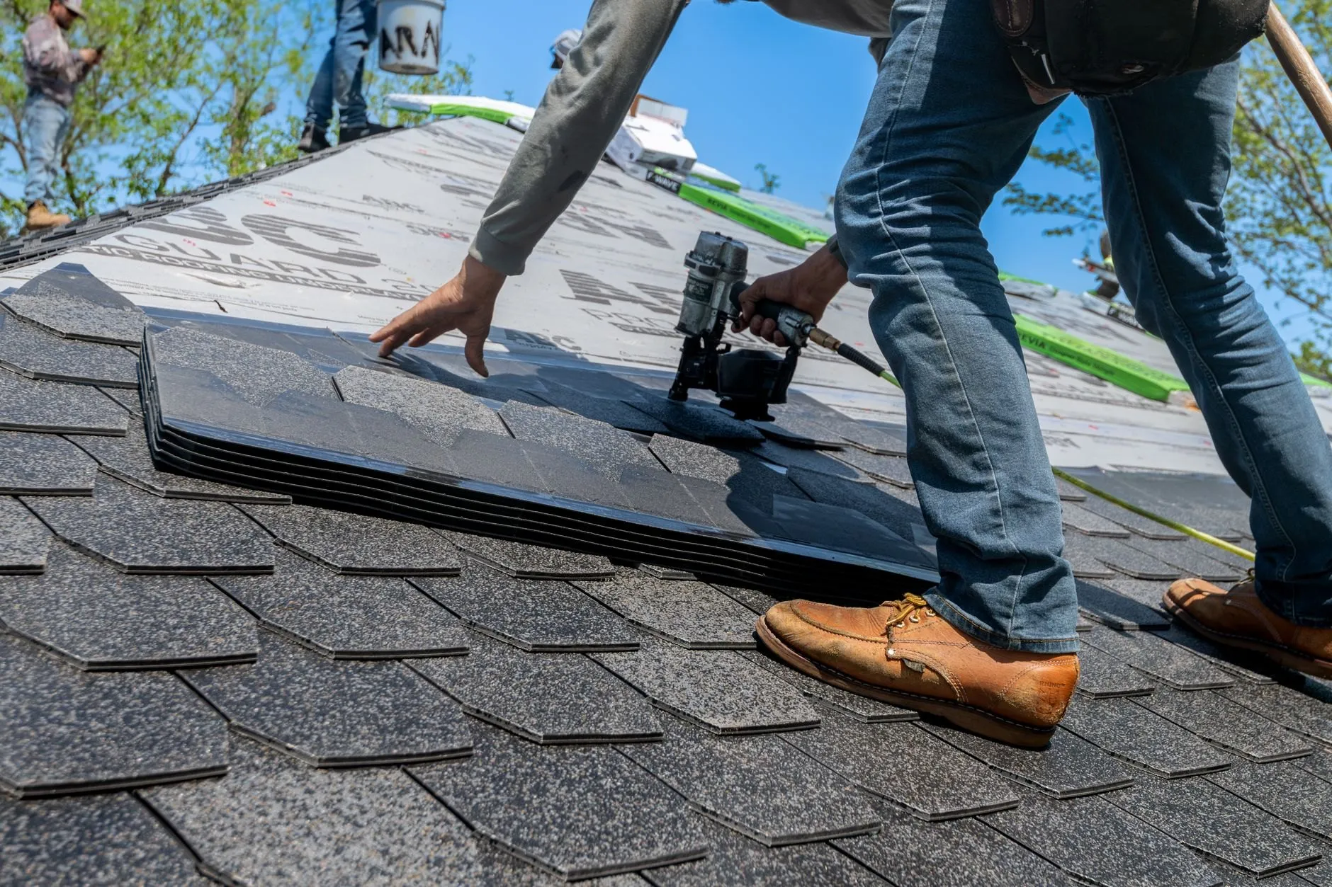 A roofer laying asphalt shingles with a nail gun